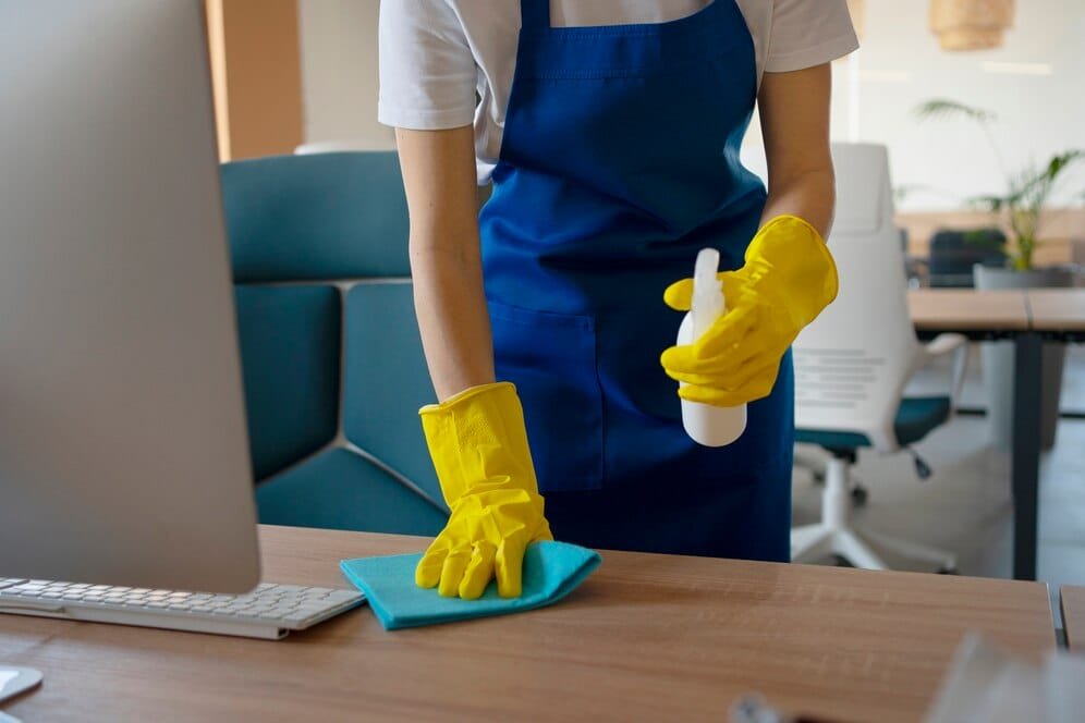 A woman in a blue apron providing house cleaning service at a desk.