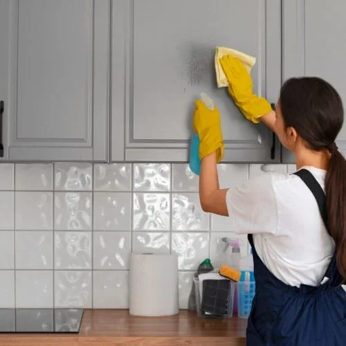 A woman wearing gloves providing house cleaning services in a kitchen near Phoenix.